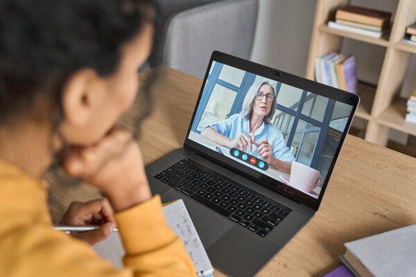 Blick �ber die Schulter auf eine junge Frau, die an ihrem Laptop sitzt und an einer Online-Beratung teilnimmt.
